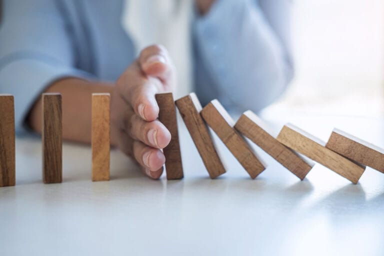 Hand stopping falling dominoes on table.