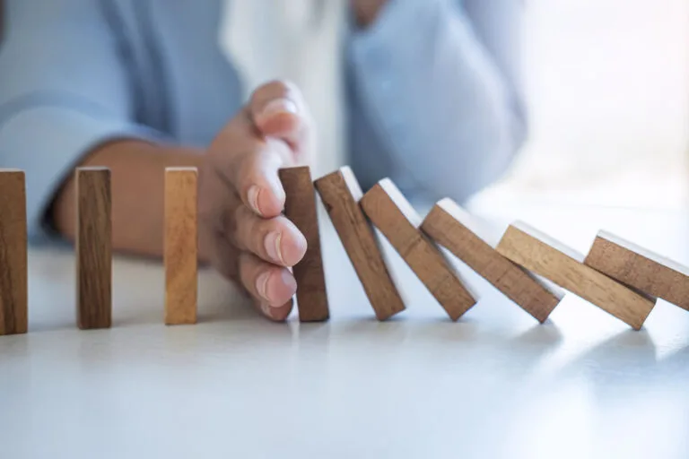 Hand stopping falling dominoes on table.