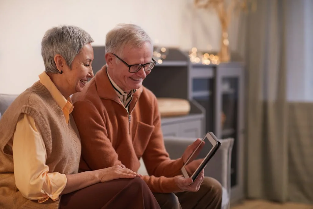 A cheerful senior couple enjoying a video call on a tablet in their cozy living room.