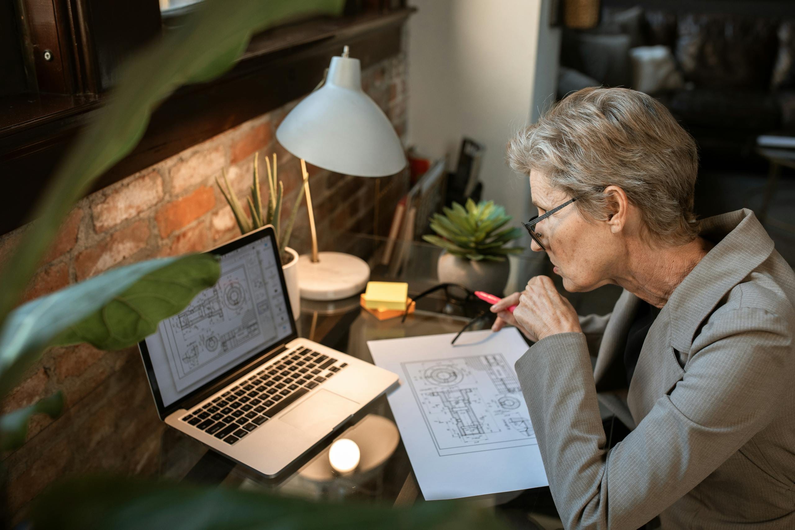 A senior engineer analyzes architectural plans on a laptop in a cozy home office.