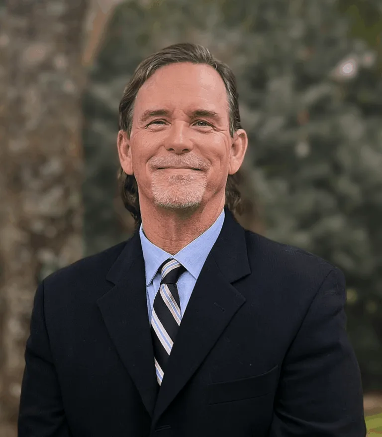 Professional man in suit smiling outdoors with greenery background