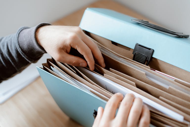 Crop unrecognizable person selecting document in opened briefcase for documents placed on wooden table